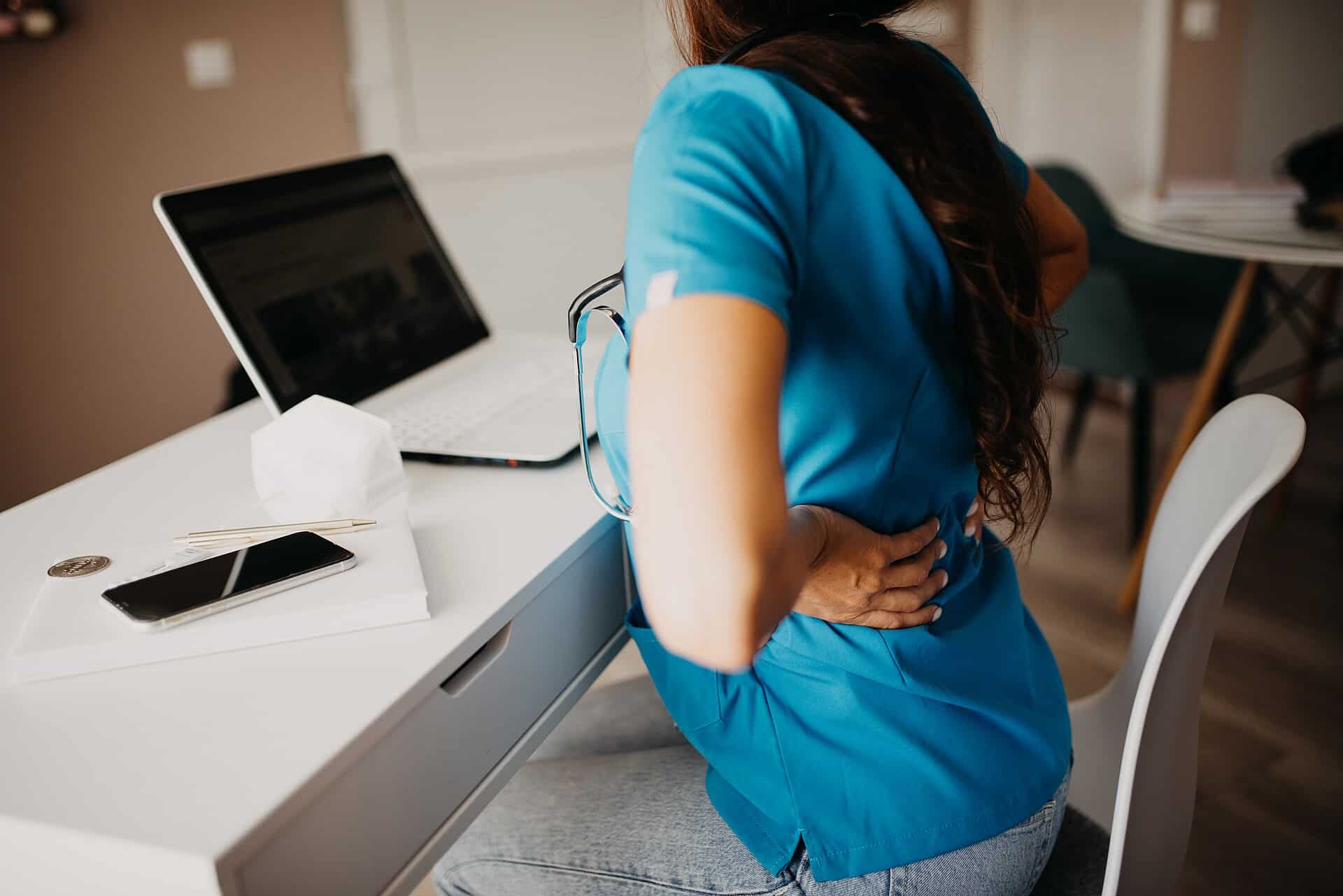 Woman holding her lower back in pain while working on a laptop