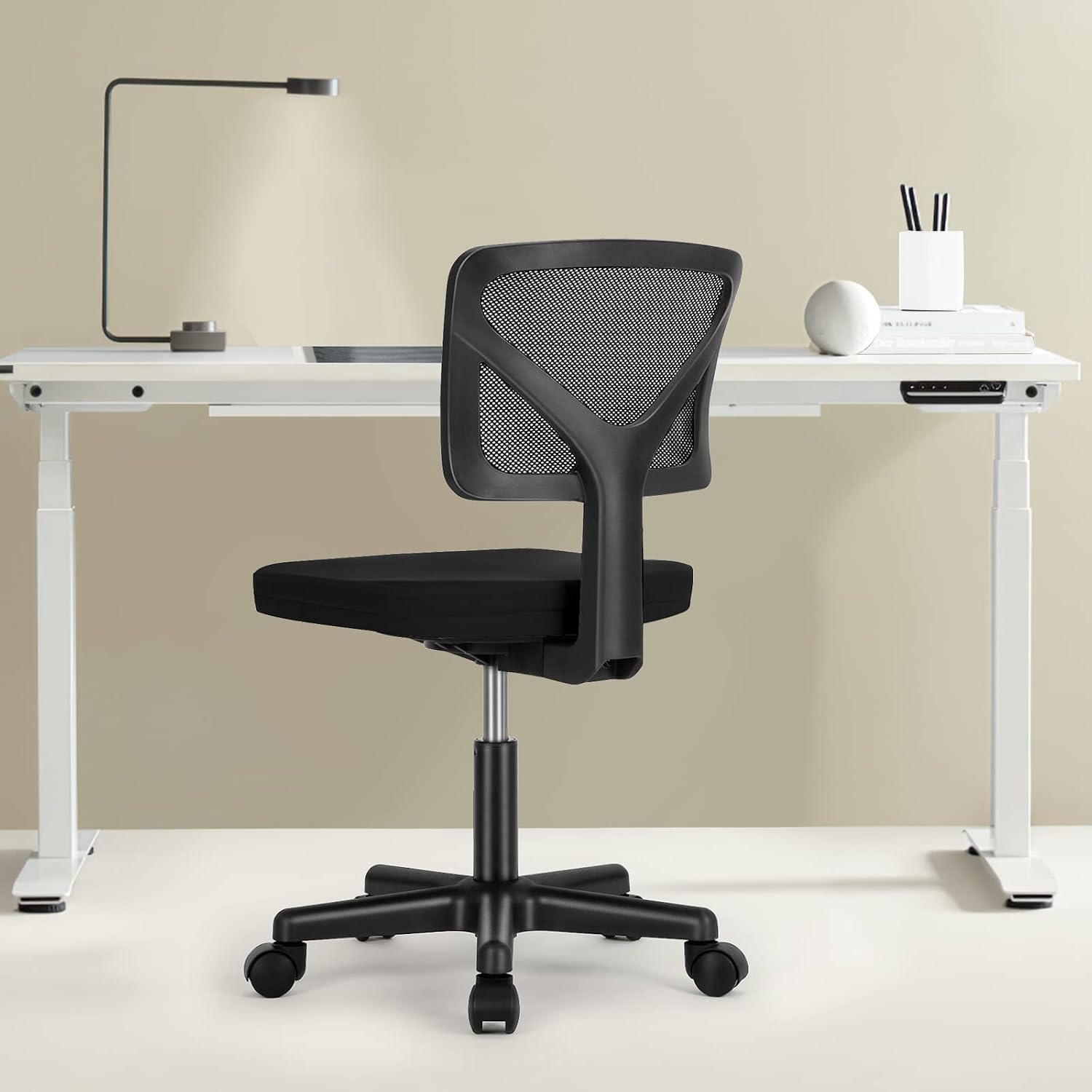 Home office desk scene with a small black armless mesh desk chair on casters in a bright room