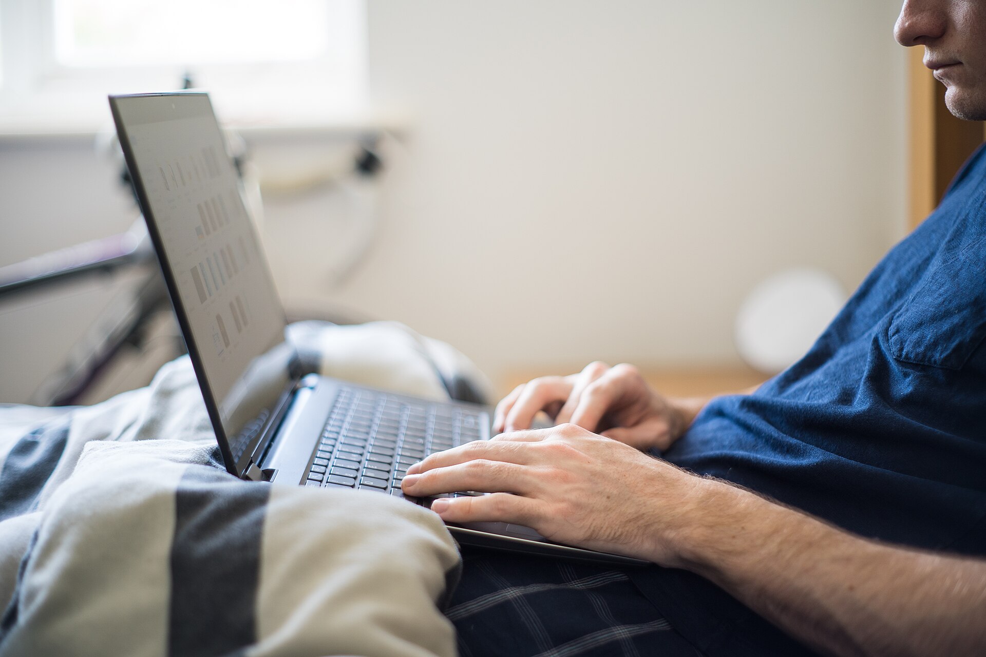 Person working on a laptop from bed during a remote work day, illustrating the need for a lap desk