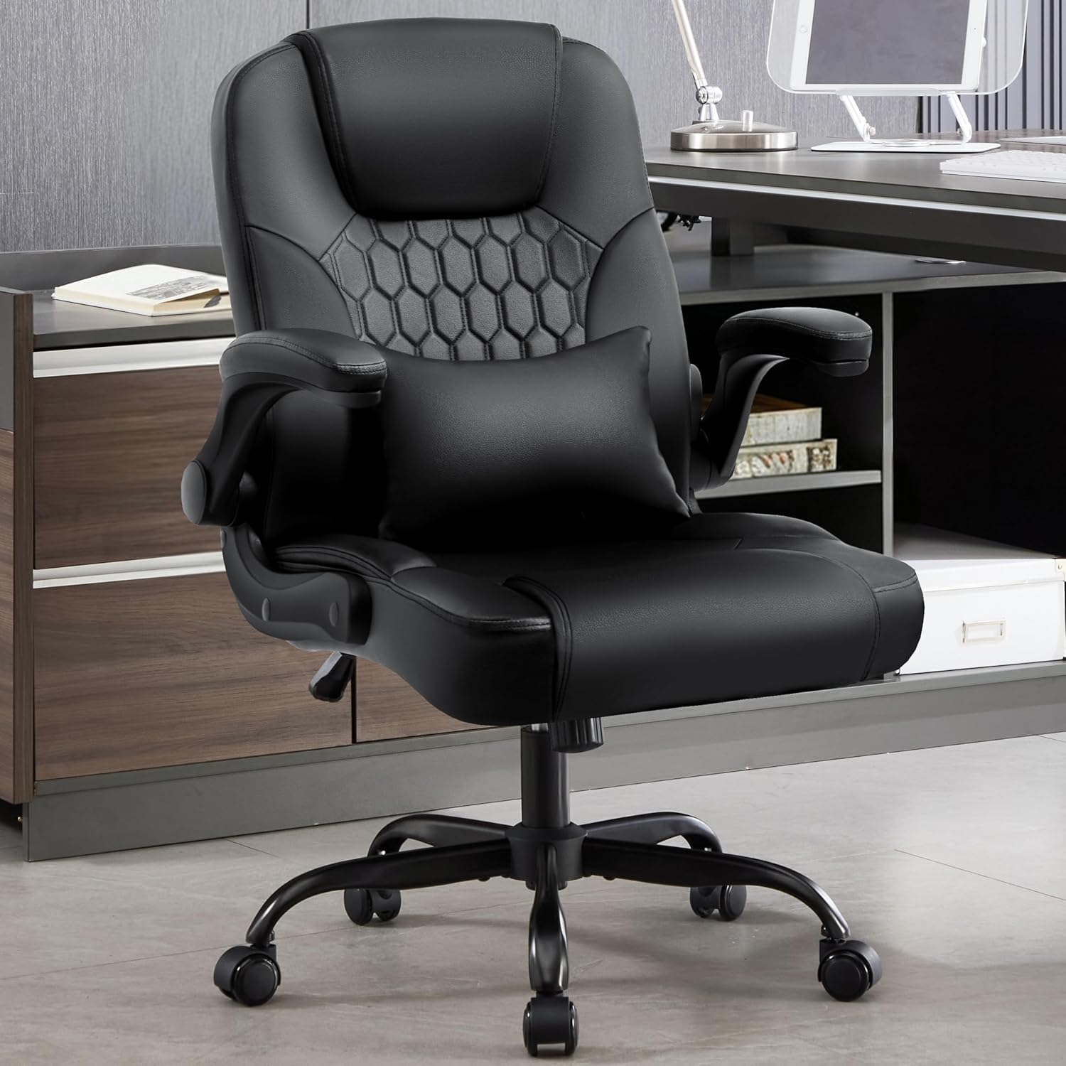 Black PU leather office chair with lumbar pillow and flip-up armrests in a dark home office