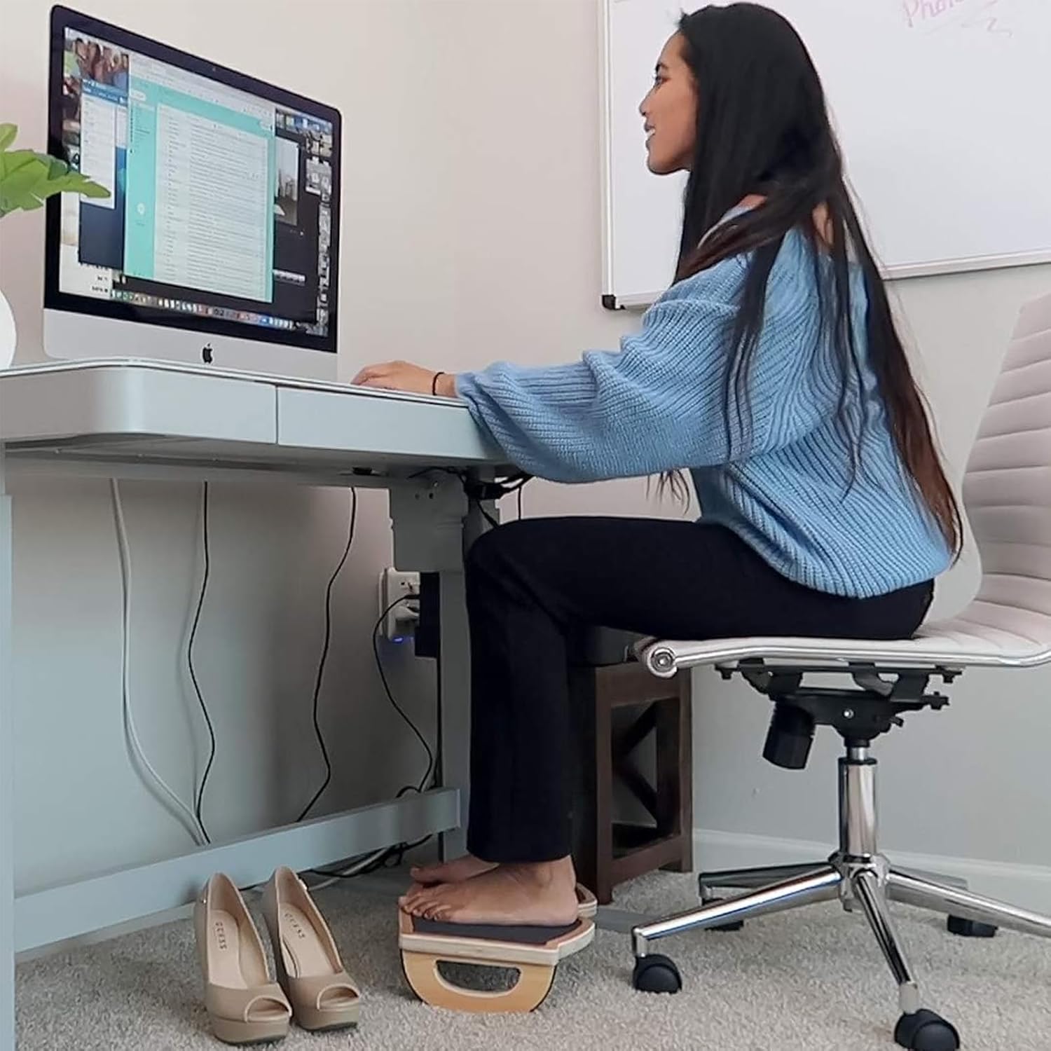 Woman sitting at a desk with both feet on a wooden rocking under-desk footrest
